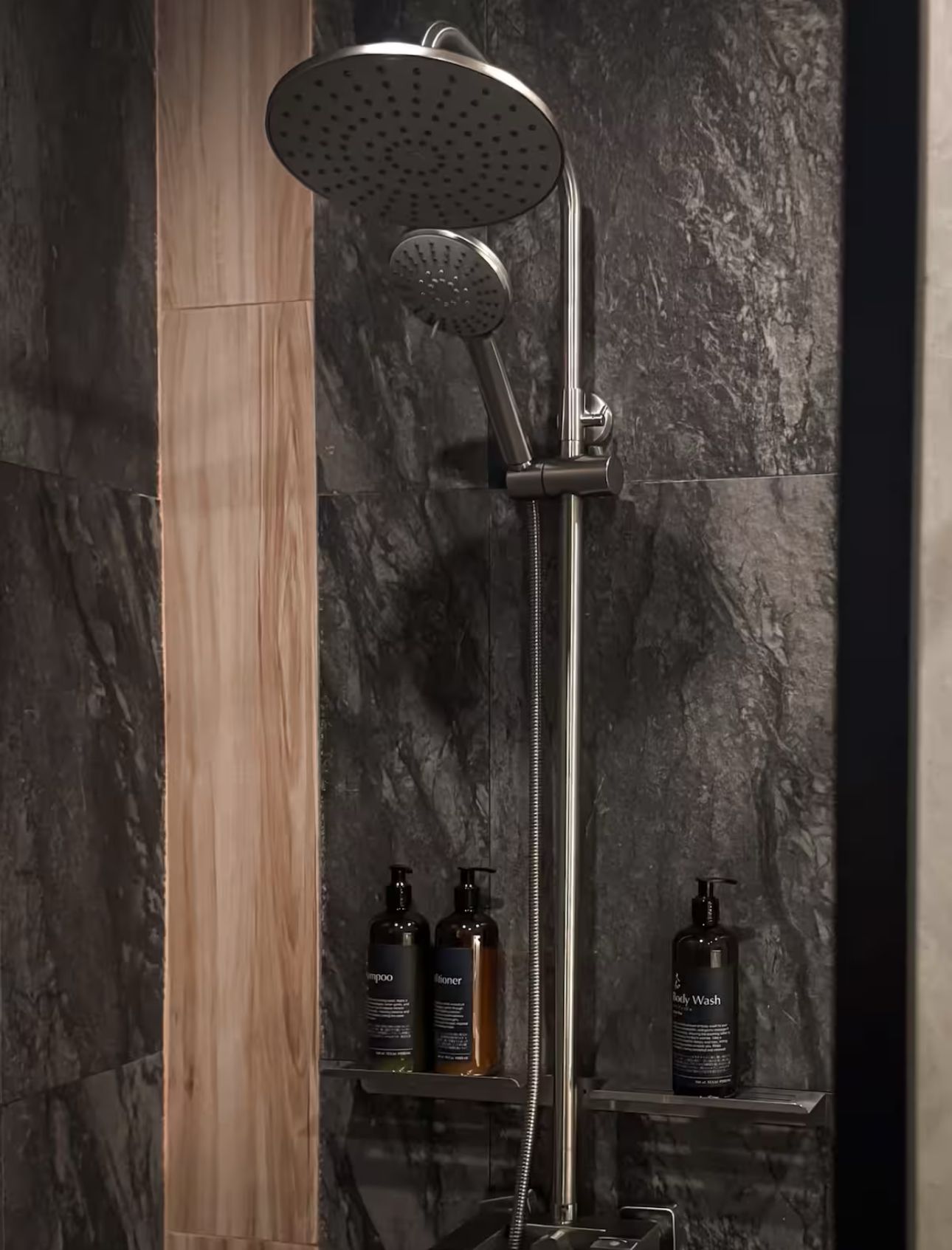 A shower head is sitting in a bathroom next to a shelf with bottles of soap.