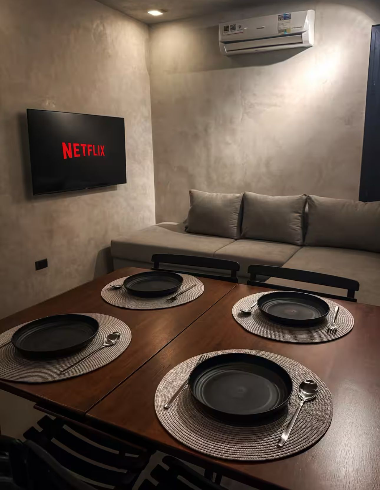 A living room with a couch , table , chairs , plates and a netflix tv on the wall.