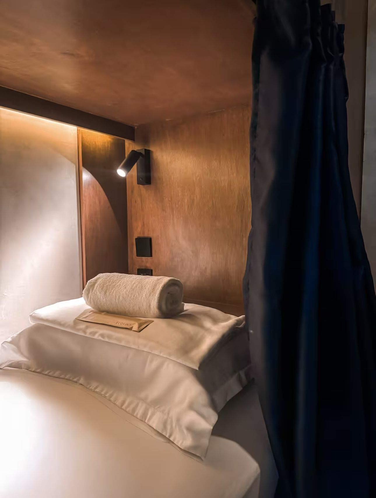 A bed with white sheets and pillows in a hotel room with a blue curtain.