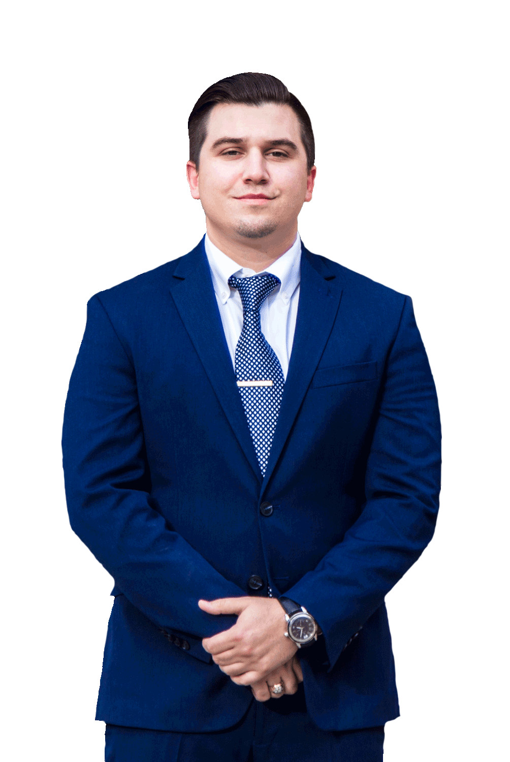 A man in a blue suit and tie is standing with his hands folded.