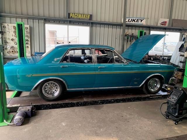 Blue classic car on a lift in a garage with the hood open.