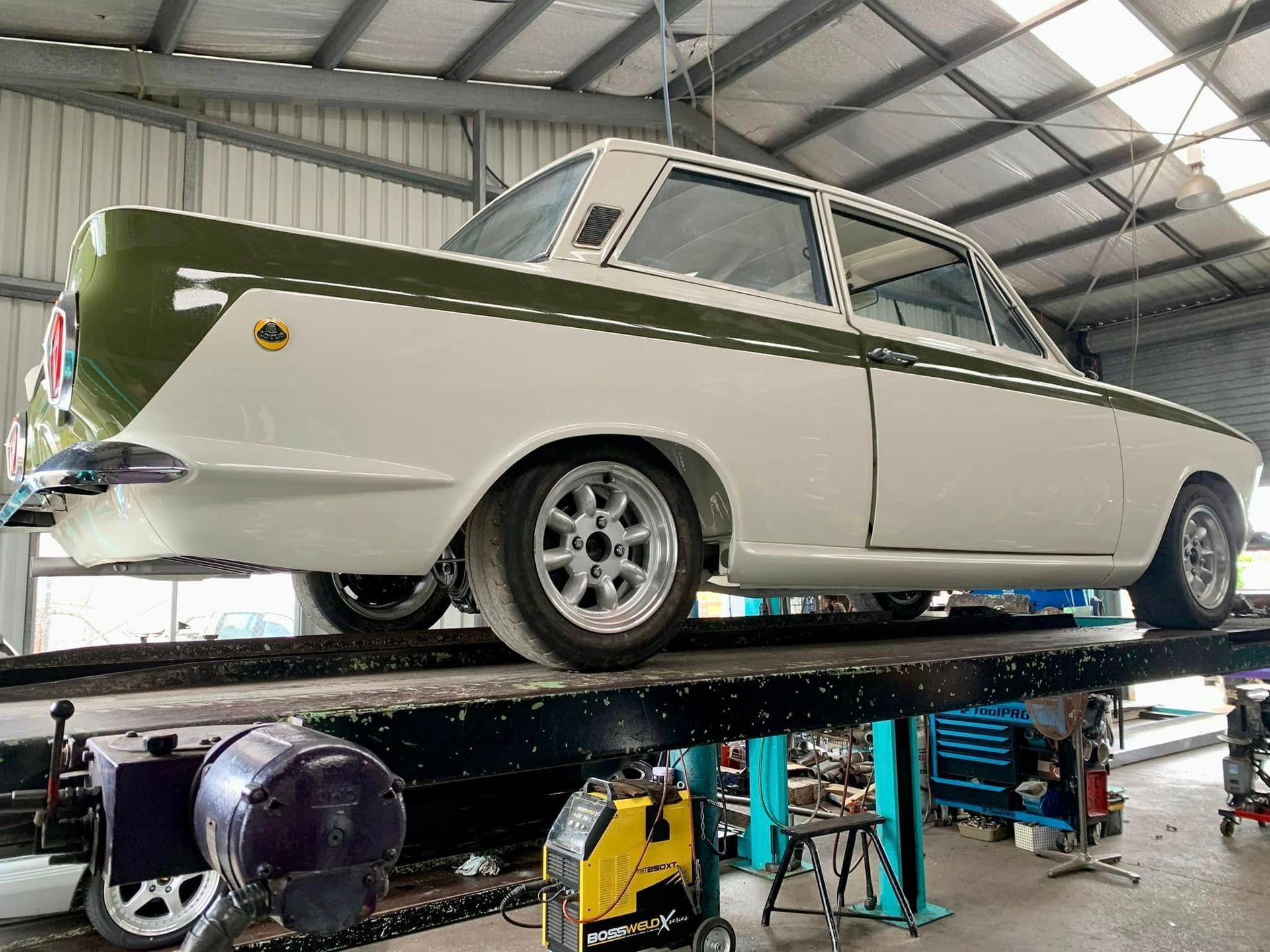 White and olive green classic car raised on a lift in a garage.— Gladstone Mufflers & Suspension In Gladstone Central, QLD