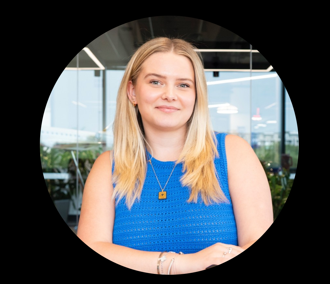 Woman in blue top, smiling, indoors, wearing necklace and bracelet.