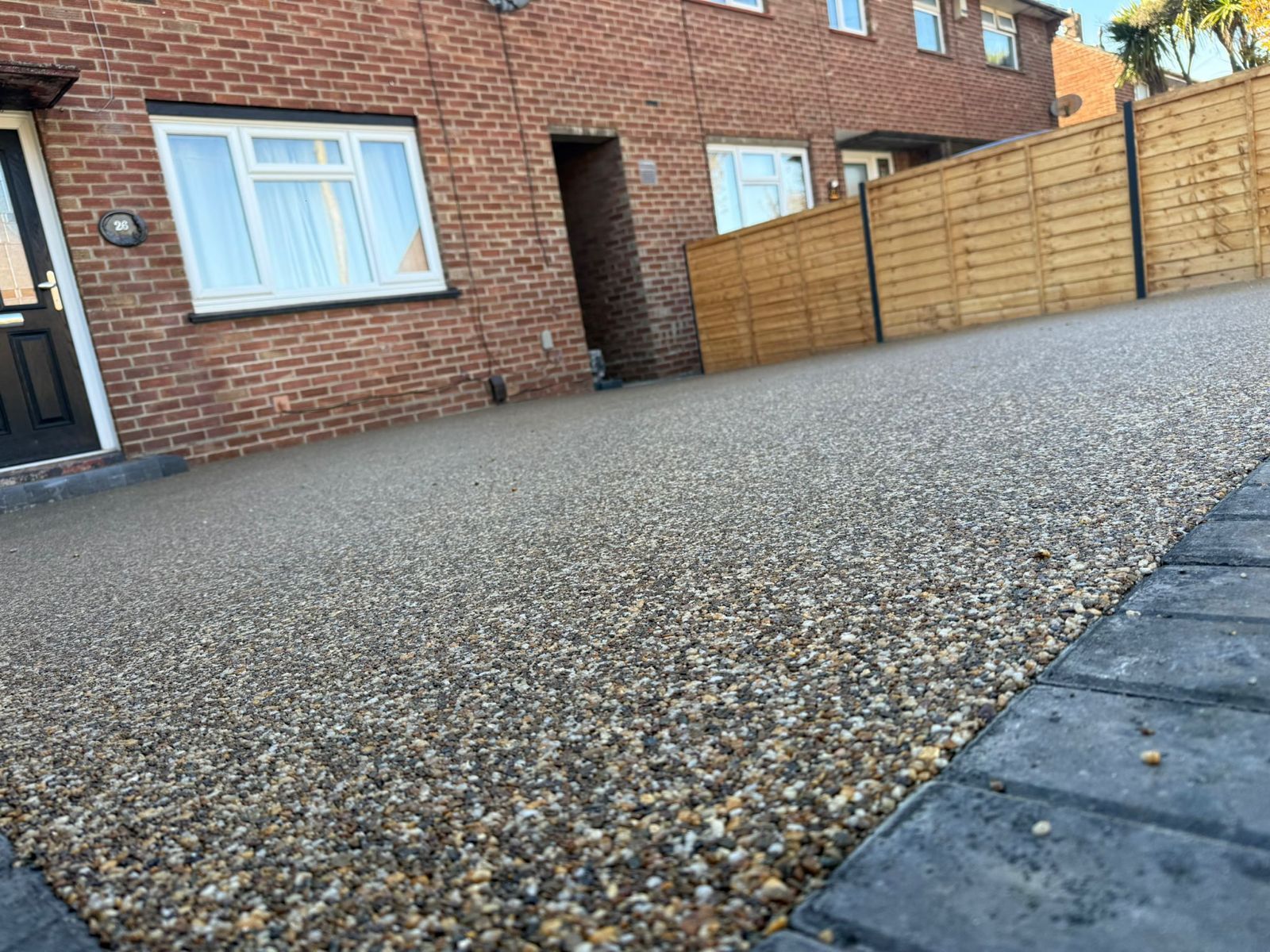 A newly laid resin-bound gravel driveway with grey block paved edging in front of a red brick house.