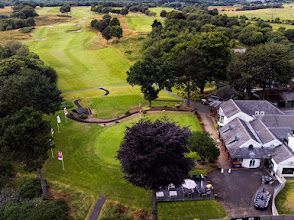 An aerial view of a golf course with a house in the middle of it.