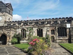 A large stone building with a clock tower and flowers in front of it.