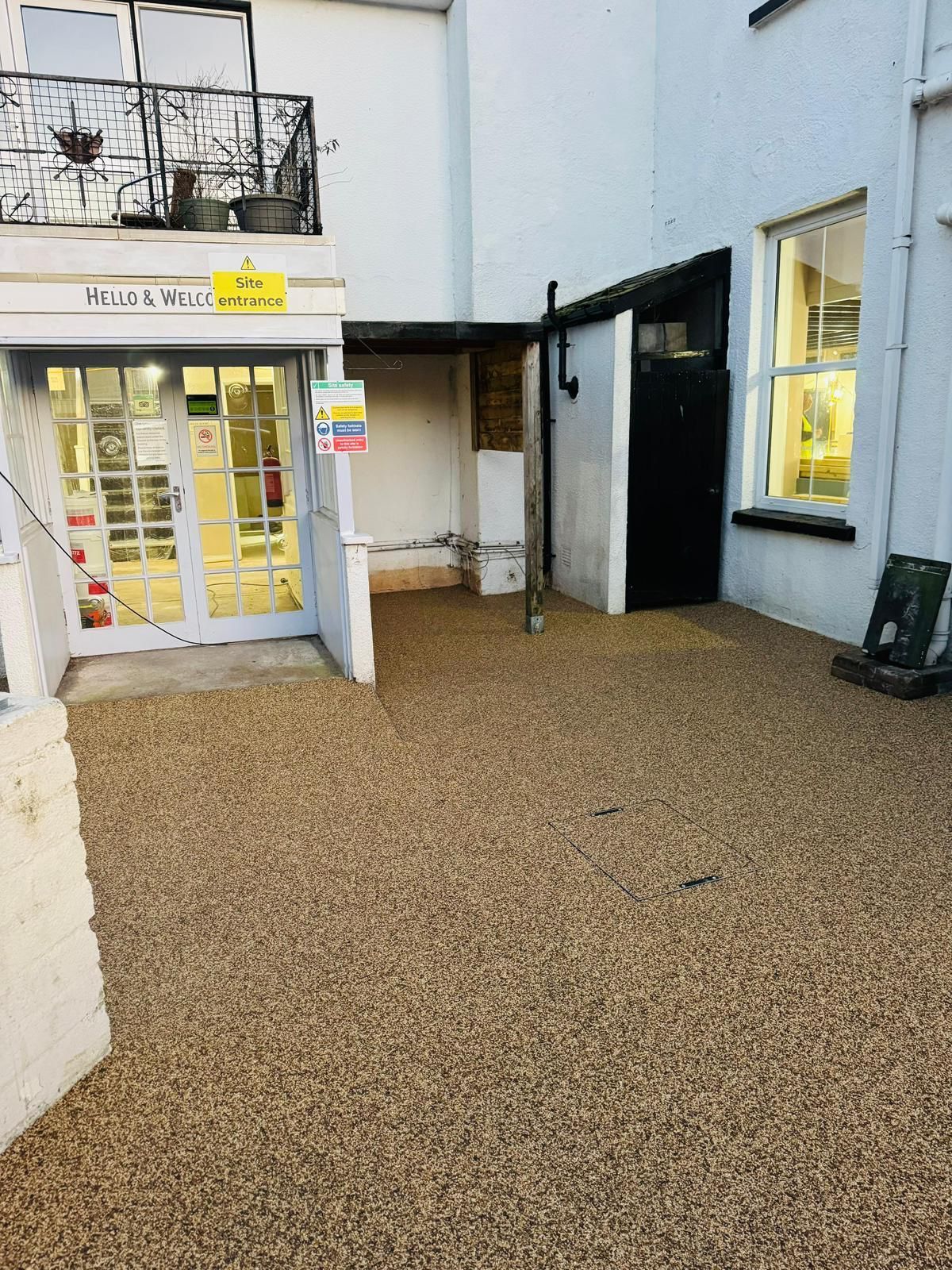 Gravel courtyard entrance to a building with glass doors and a dark door, beneath white exterior.