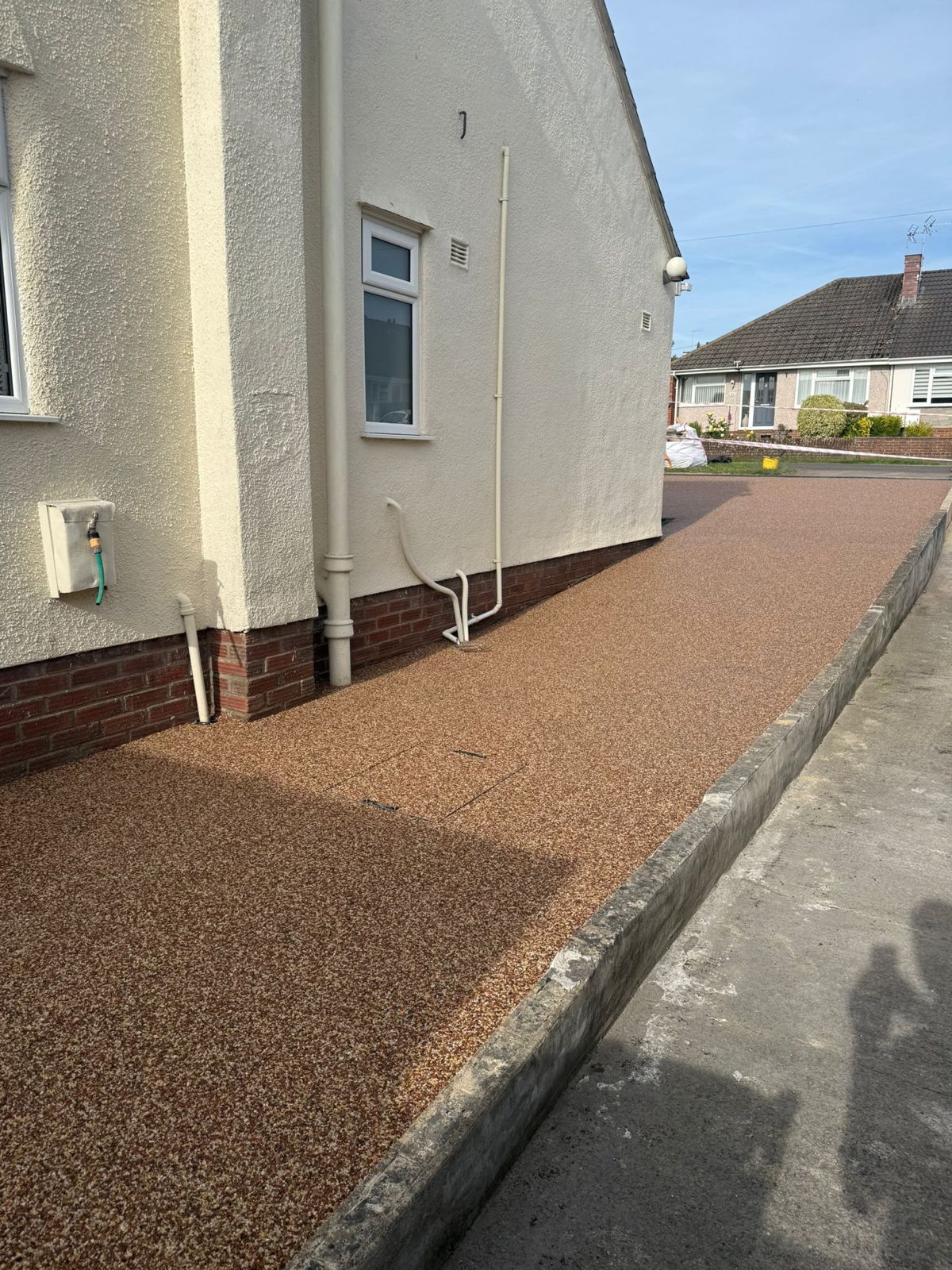 Gravel path beside a white house in a residential neighborhood, with a curb and street visible.