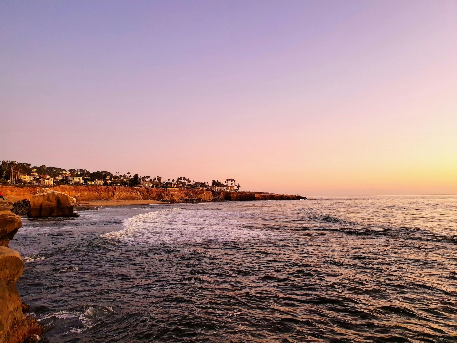 A sunset over the ocean with a cliff in the foreground