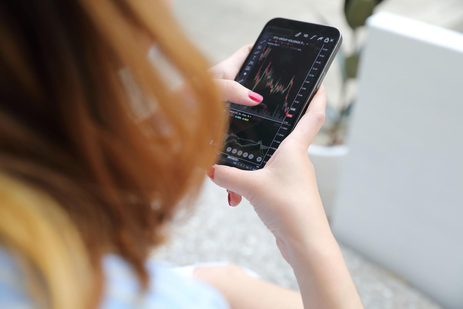 Frau nicht vollständig sichtbar hält ein Smartphone mit Börsen Chartdaten, zur Verdeutlichung der Überprüfung von Wertentwicklungen