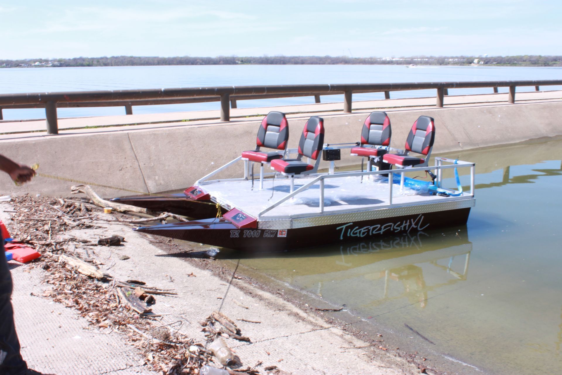 Small pontoon boat with four seats on the water near a concrete bank.
