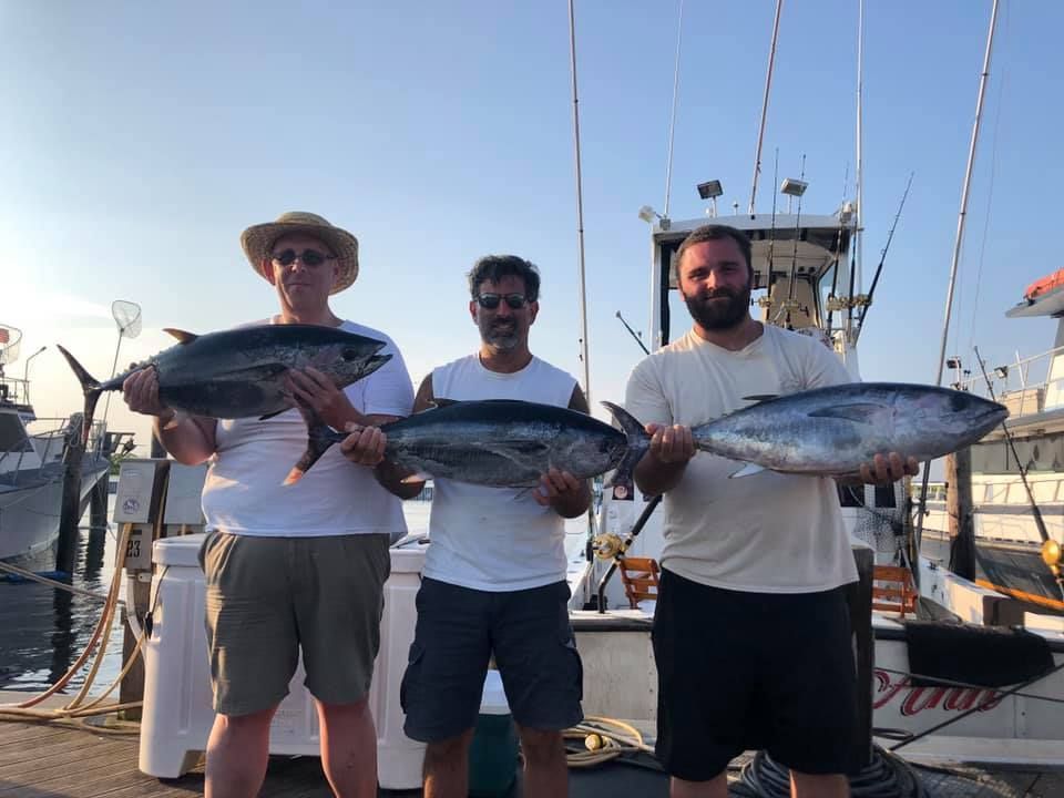 three men holding tuna