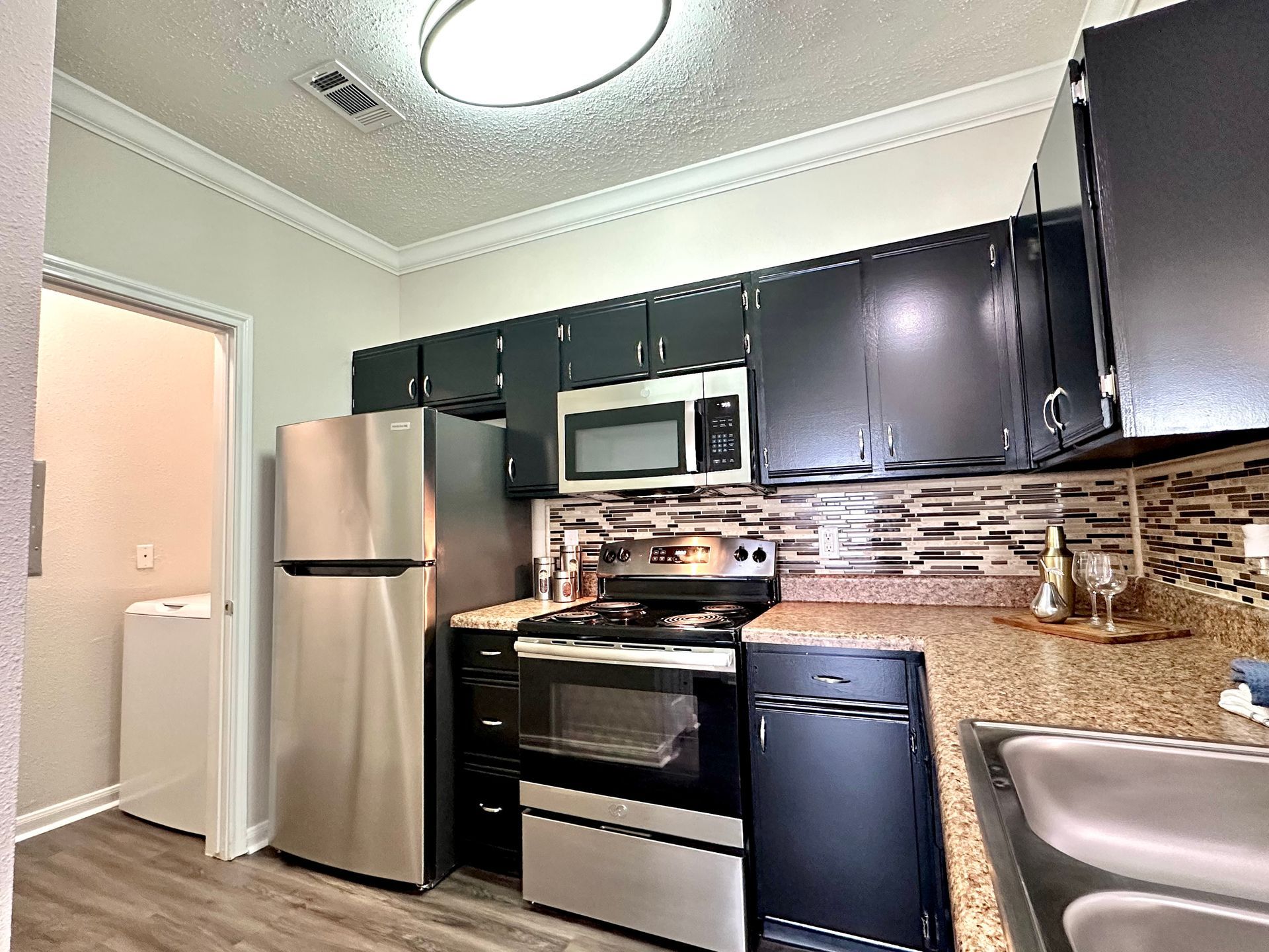 Kitchen with stainless steel appliances, dark cabinets, and patterned backsplash.