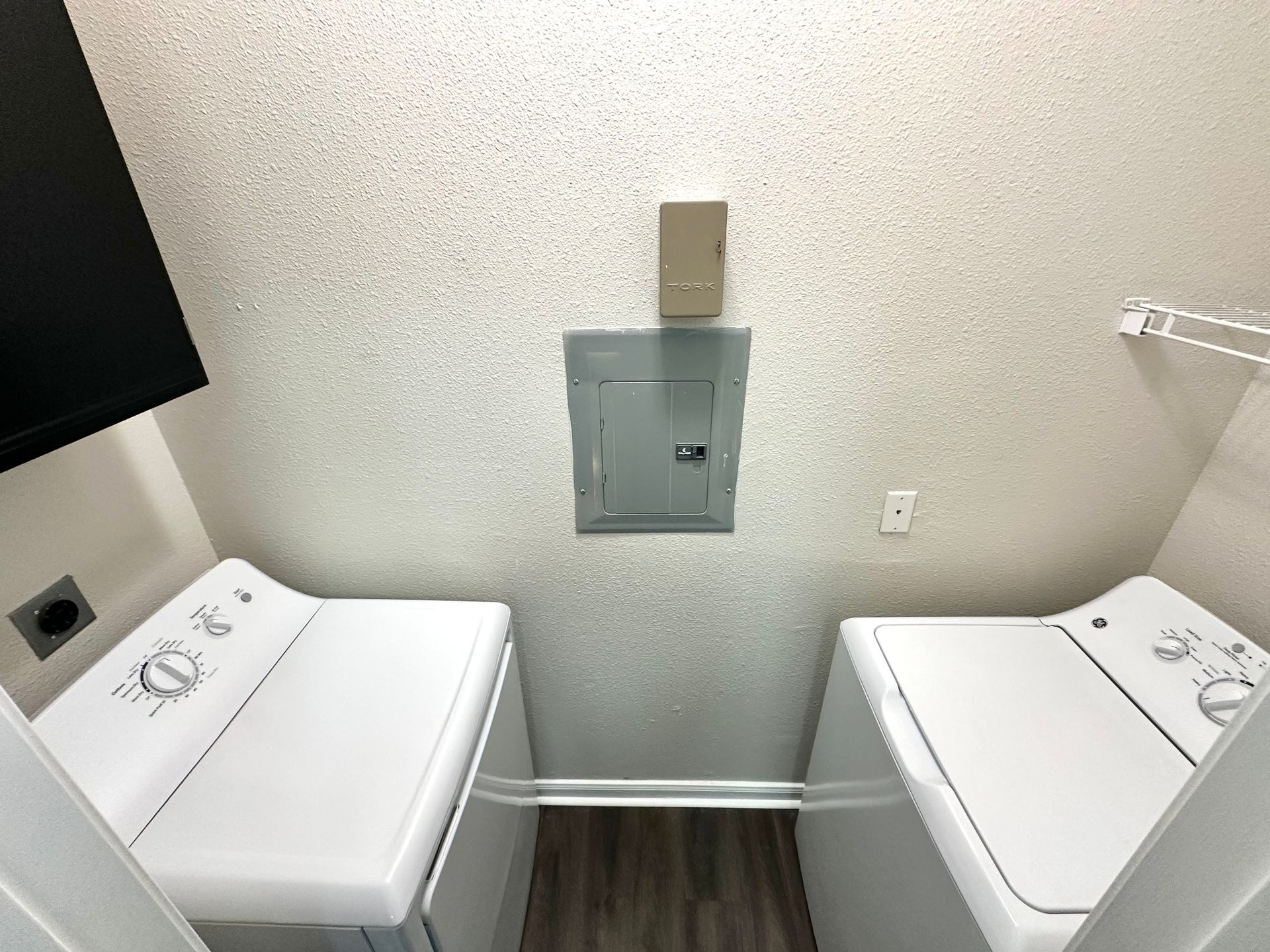 Laundry room with white washer and dryer, electrical panel, and textured walls.