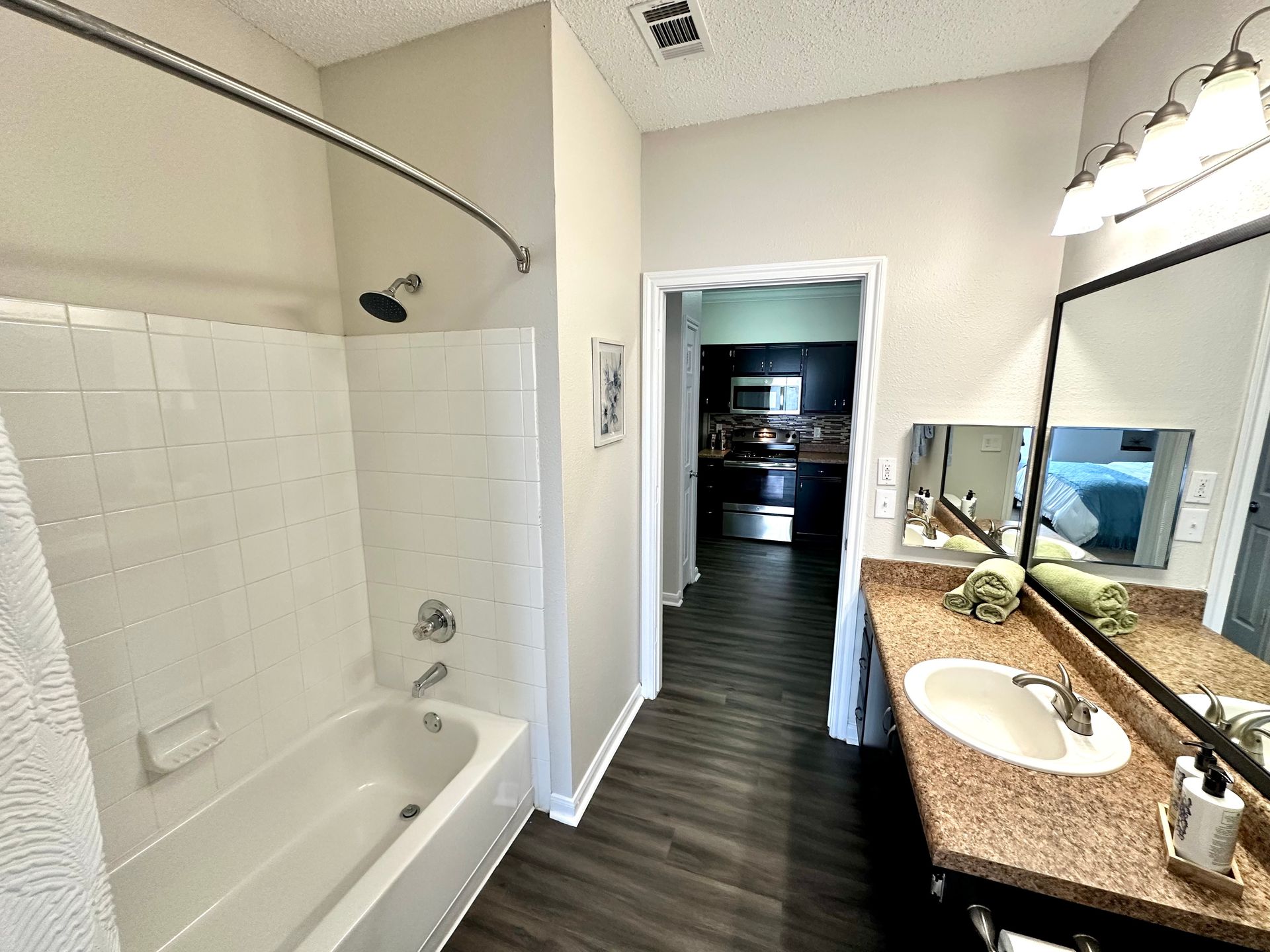 Bathroom with bathtub, sink, and doorway to kitchen. Dark flooring, white tile, neutral walls.
