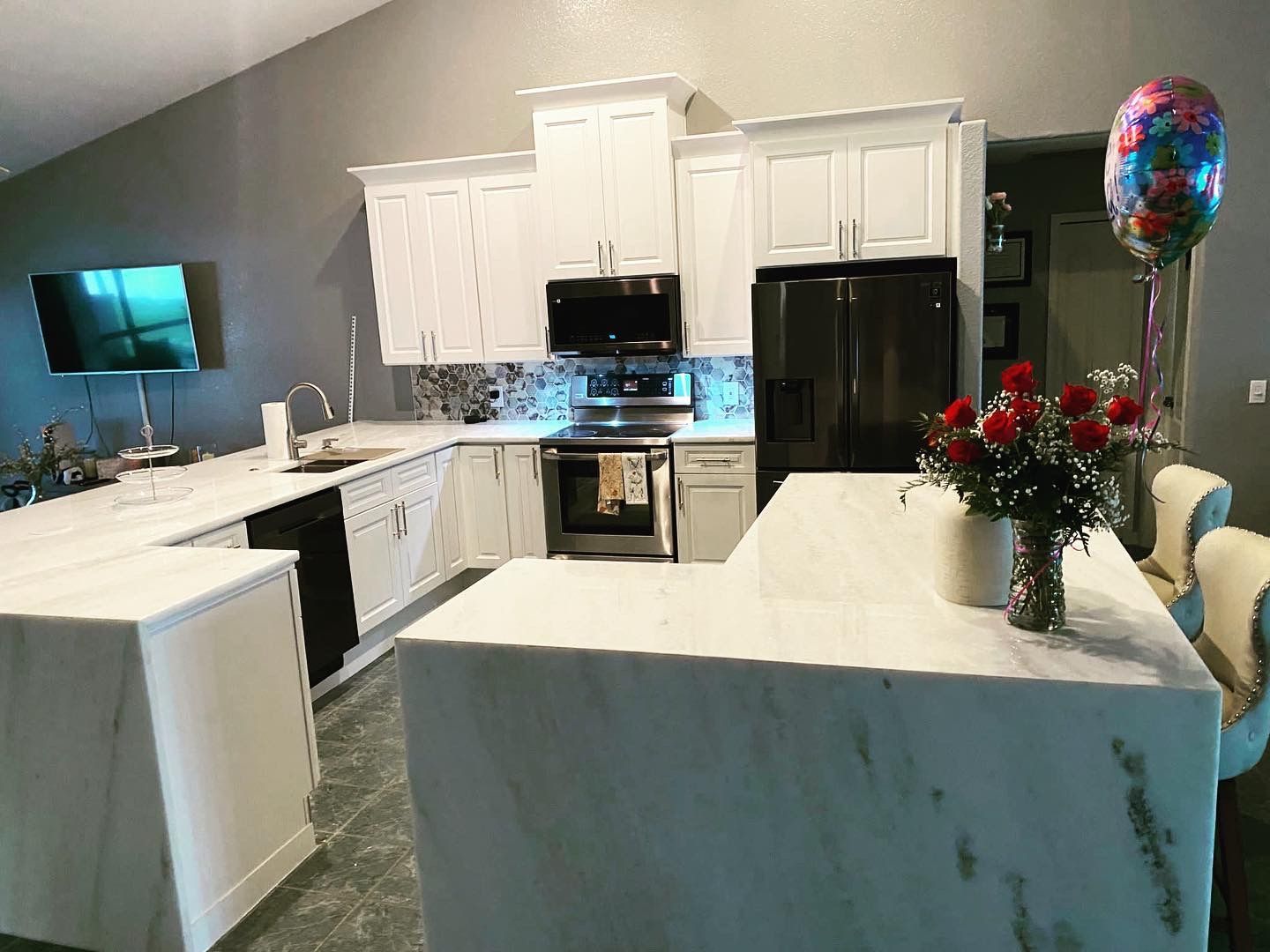 A kitchen with white cabinets , stainless steel appliances , and a large island.