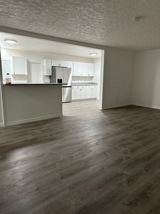 A living room with hardwood floors and a kitchen in the background.