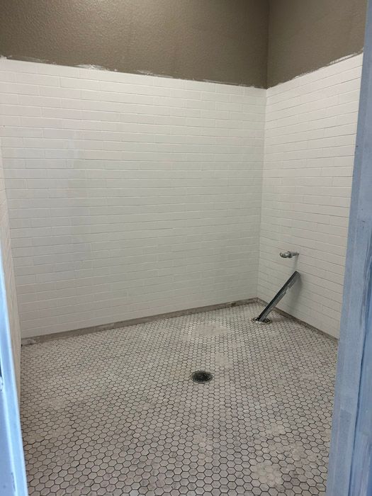 A bathroom with white tiles and a drain in the floor.