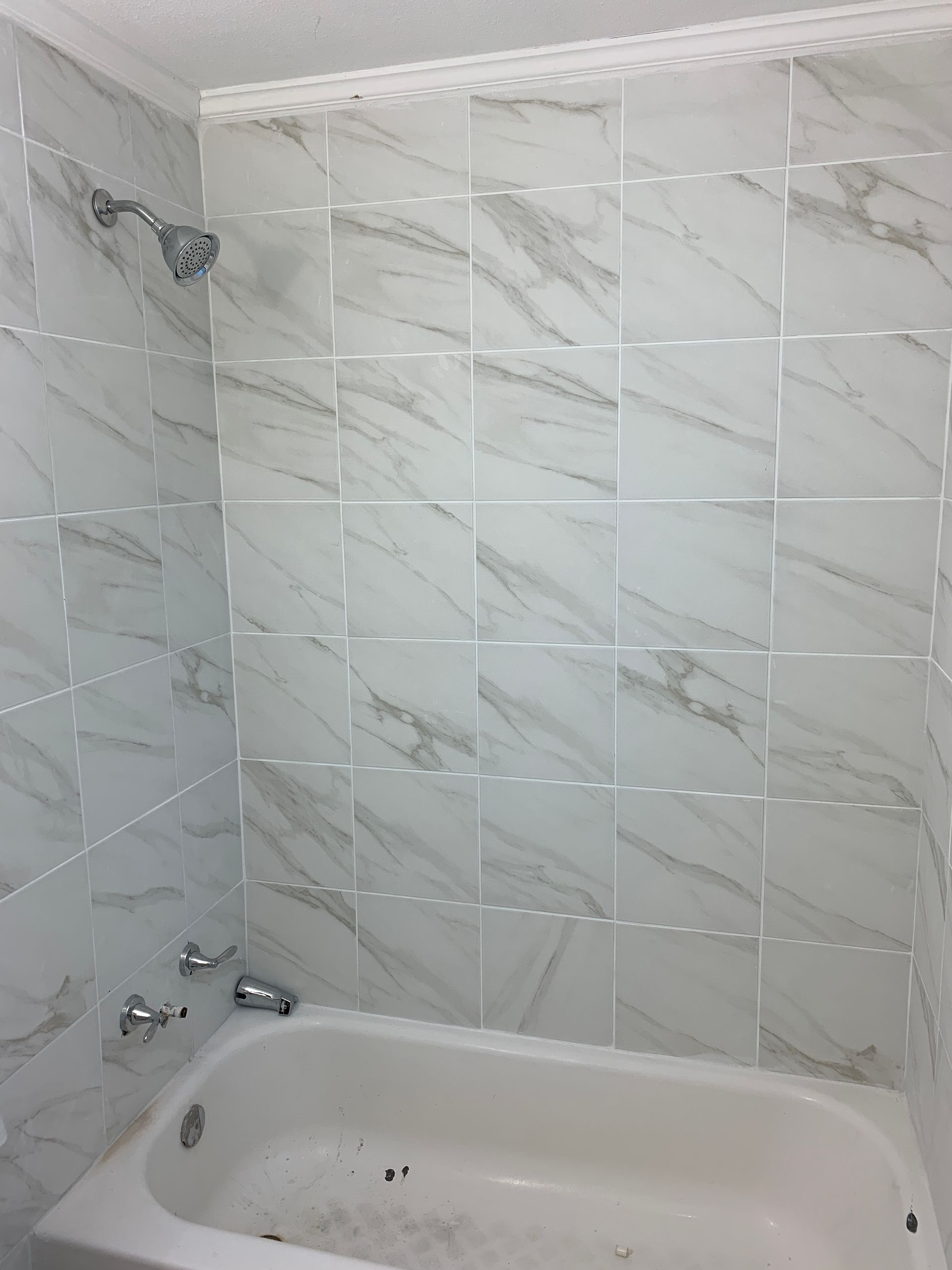 A bathtub in a bathroom with marble tiles and a shower head.