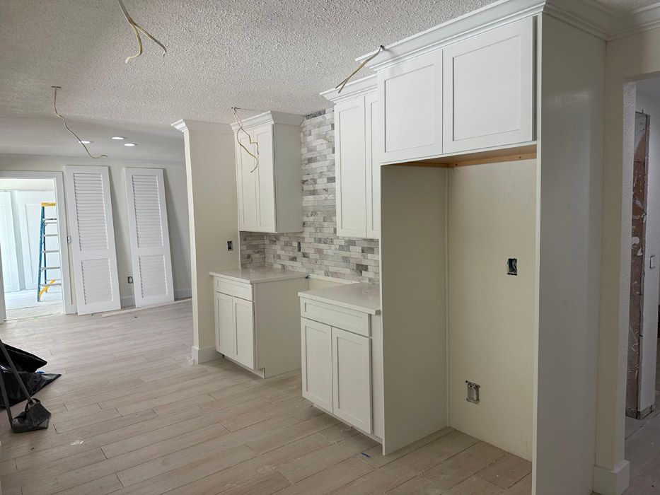 A kitchen under construction with white cabinets and a refrigerator.
