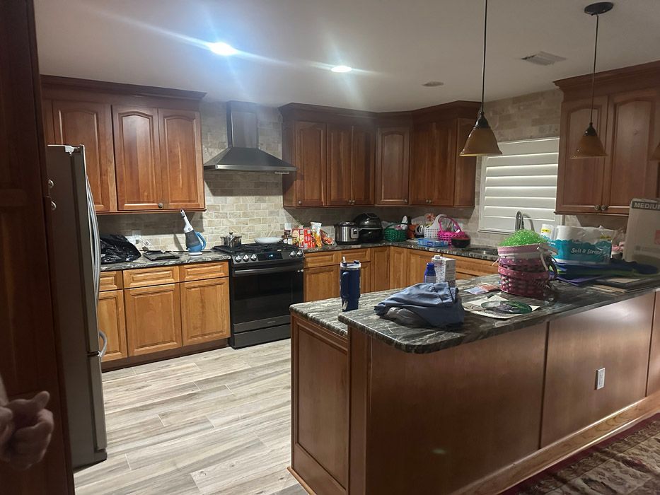 A kitchen with wooden cabinets , granite counter tops , a refrigerator , stove and sink.