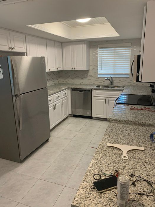 A kitchen with stainless steel appliances , granite counter tops , white cabinets and a refrigerator.