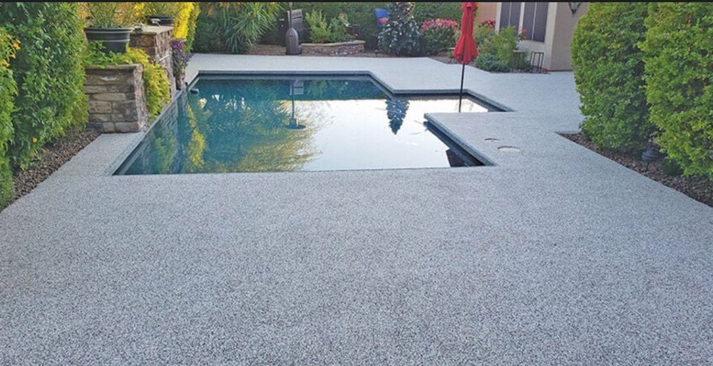 A large swimming pool is surrounded by a concrete patio and a red umbrella.