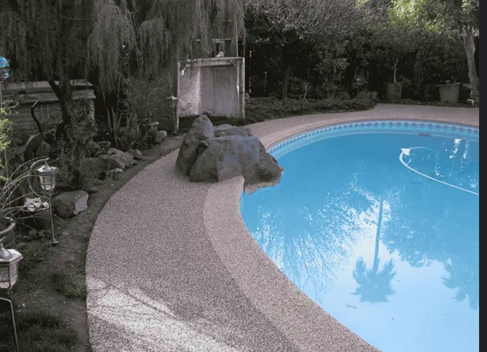 A large swimming pool surrounded by rocks and trees in a backyard.
