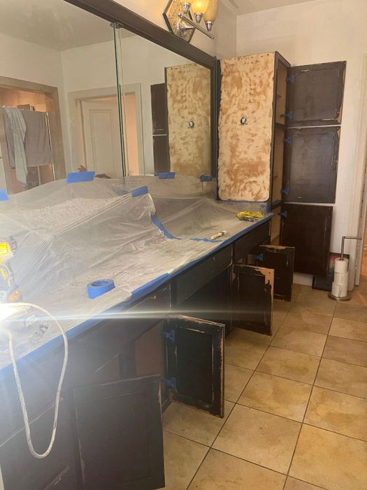 A bathroom with a large mirror and cabinets being painted.