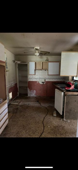 An empty kitchen with a sink , cabinets , and a ceiling fan.