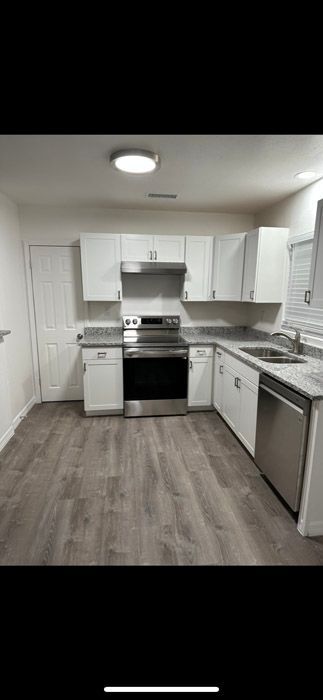 A kitchen with white cabinets , stainless steel appliances , a sink , and a stove.
