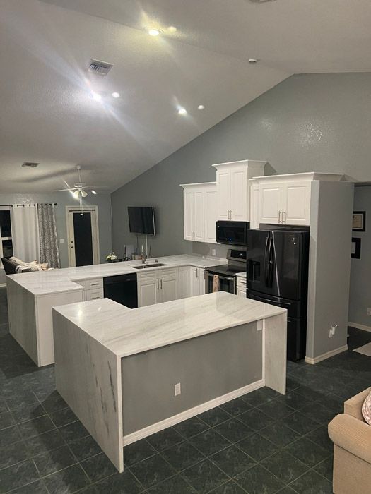 A kitchen with white cabinets , a black refrigerator , and a large island.