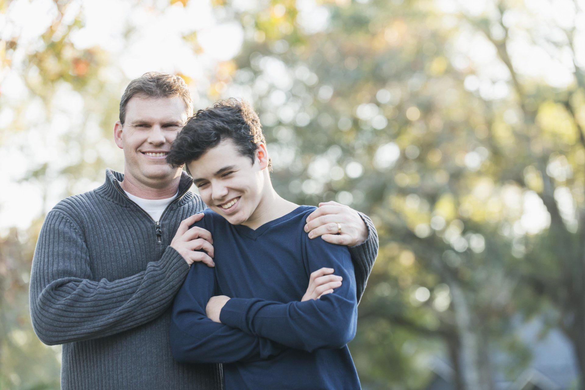 A father is holding his teenage son at the shoulders and they are smiling