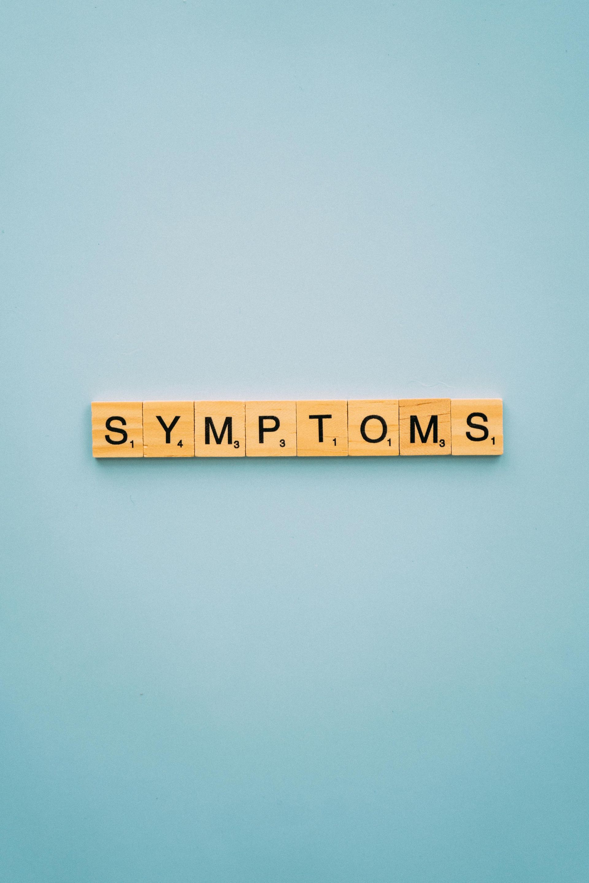 The word "symptoms" is laid out in scrabble letters on a table