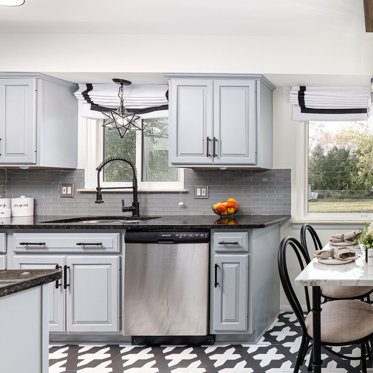 A kitchen with gray cabinets , stainless steel appliances , a sink , and a table.