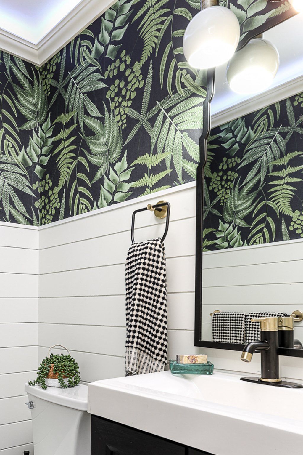 A bathroom with a sink , toilet , mirror and tropical wallpaper.