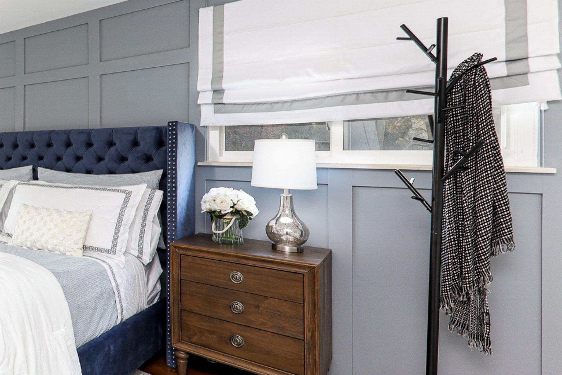 A bedroom with a bed , nightstand , lamp and coat rack.