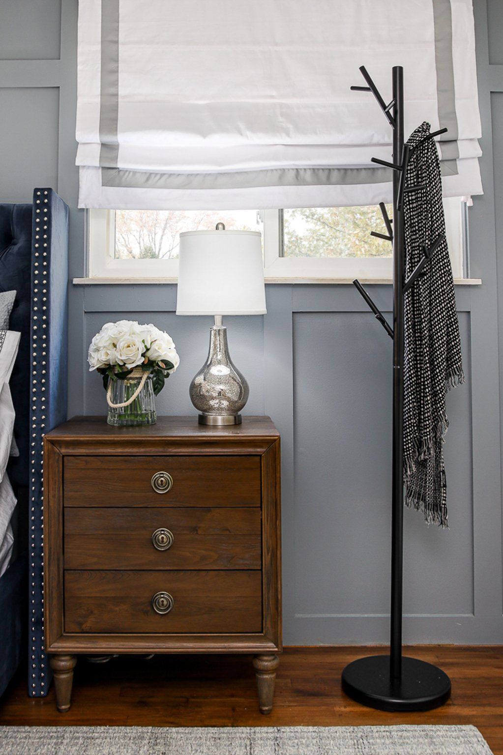 A bedroom with a nightstand , lamp , and coat rack.