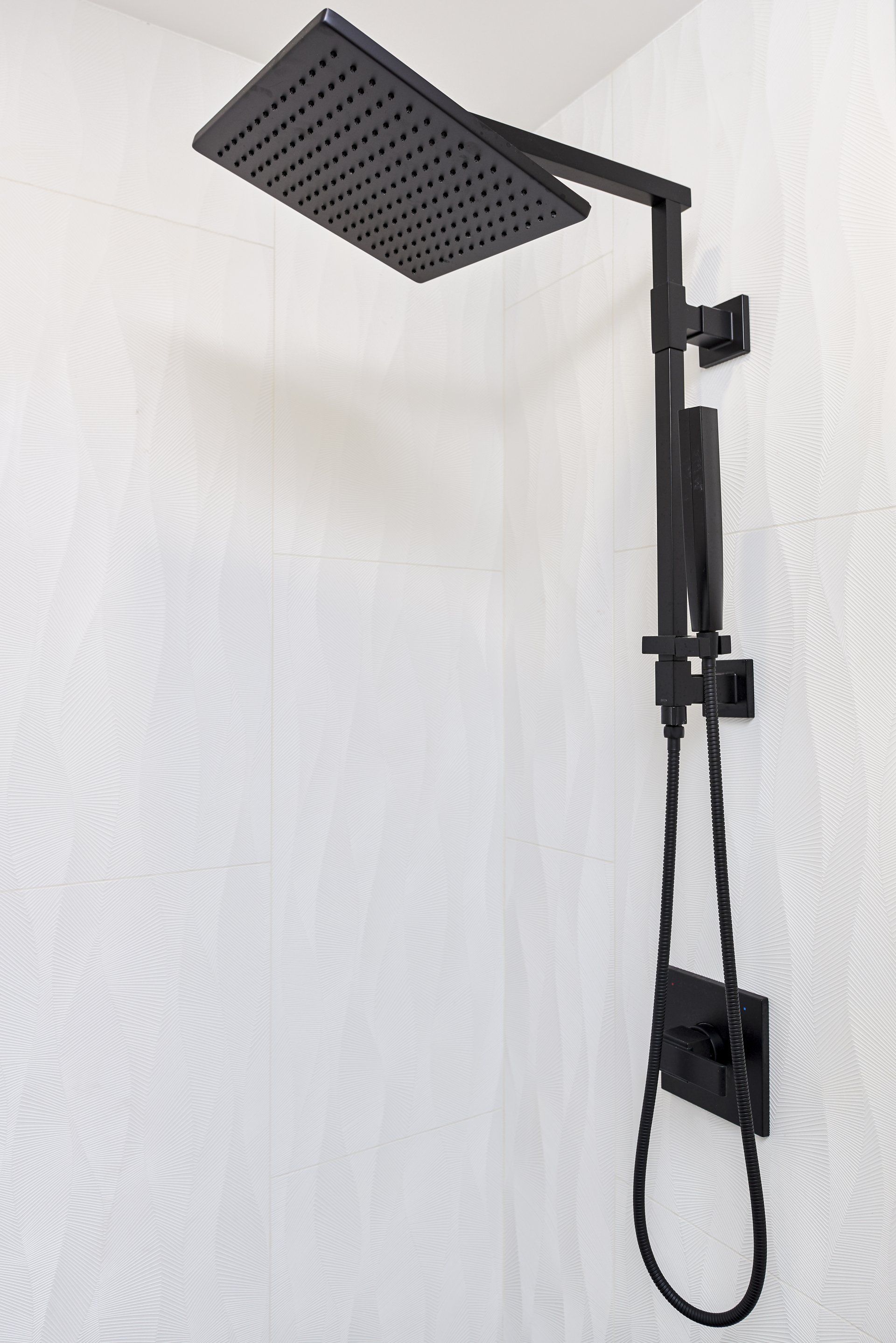 A black shower head is hanging on a white wall in a bathroom.
