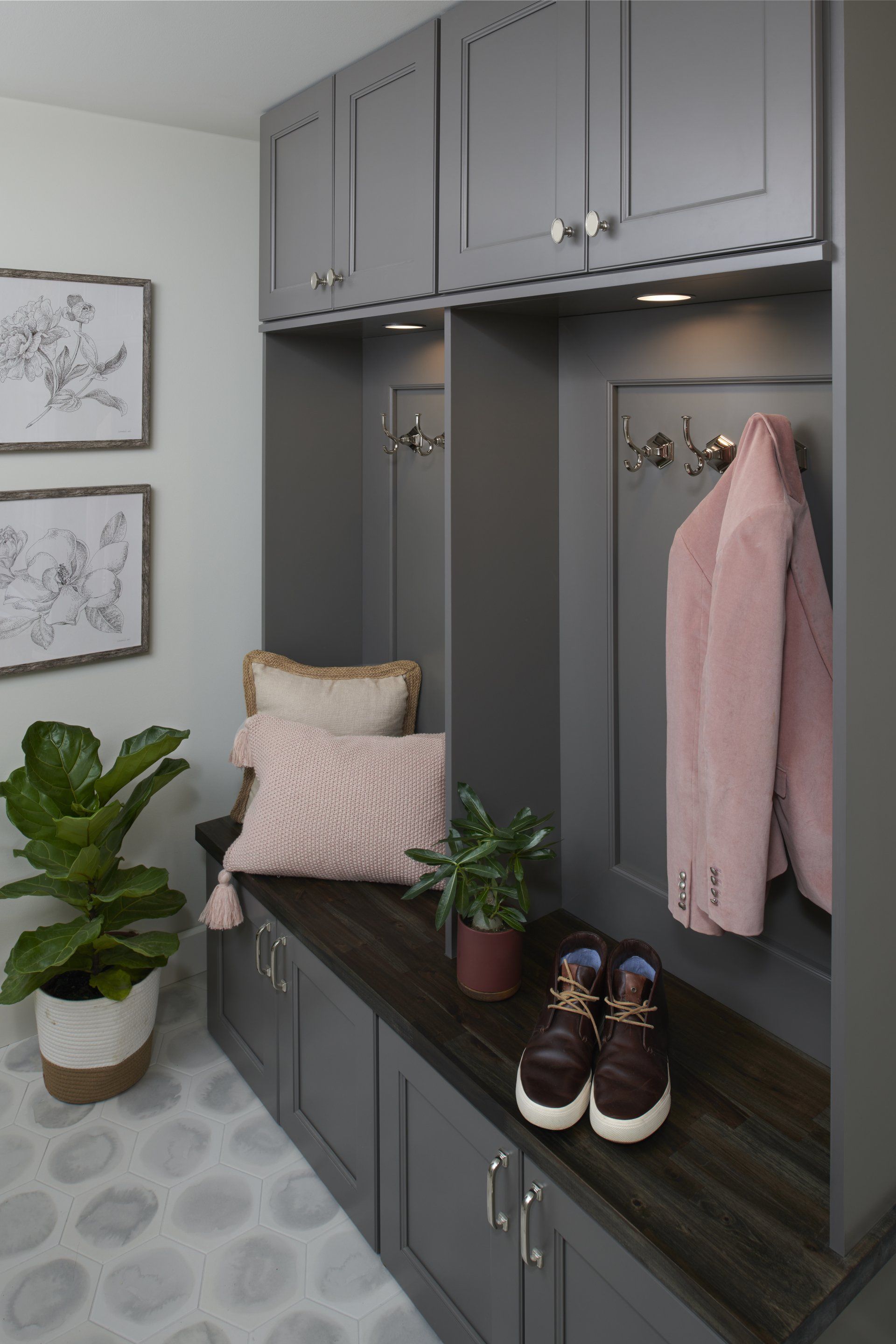 A mud room with gray cabinets and a pink coat hanging on the wall.