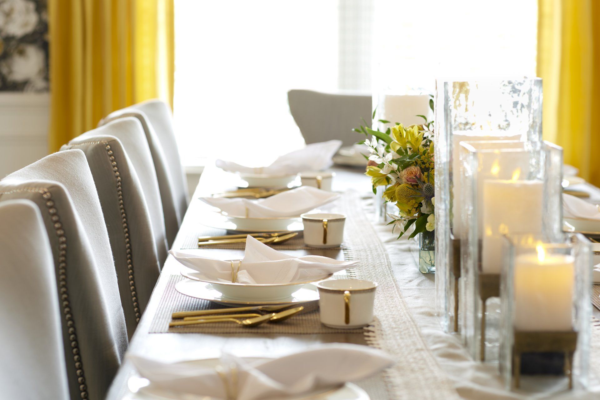 A long dining table with plates , bowls , silverware and candles.