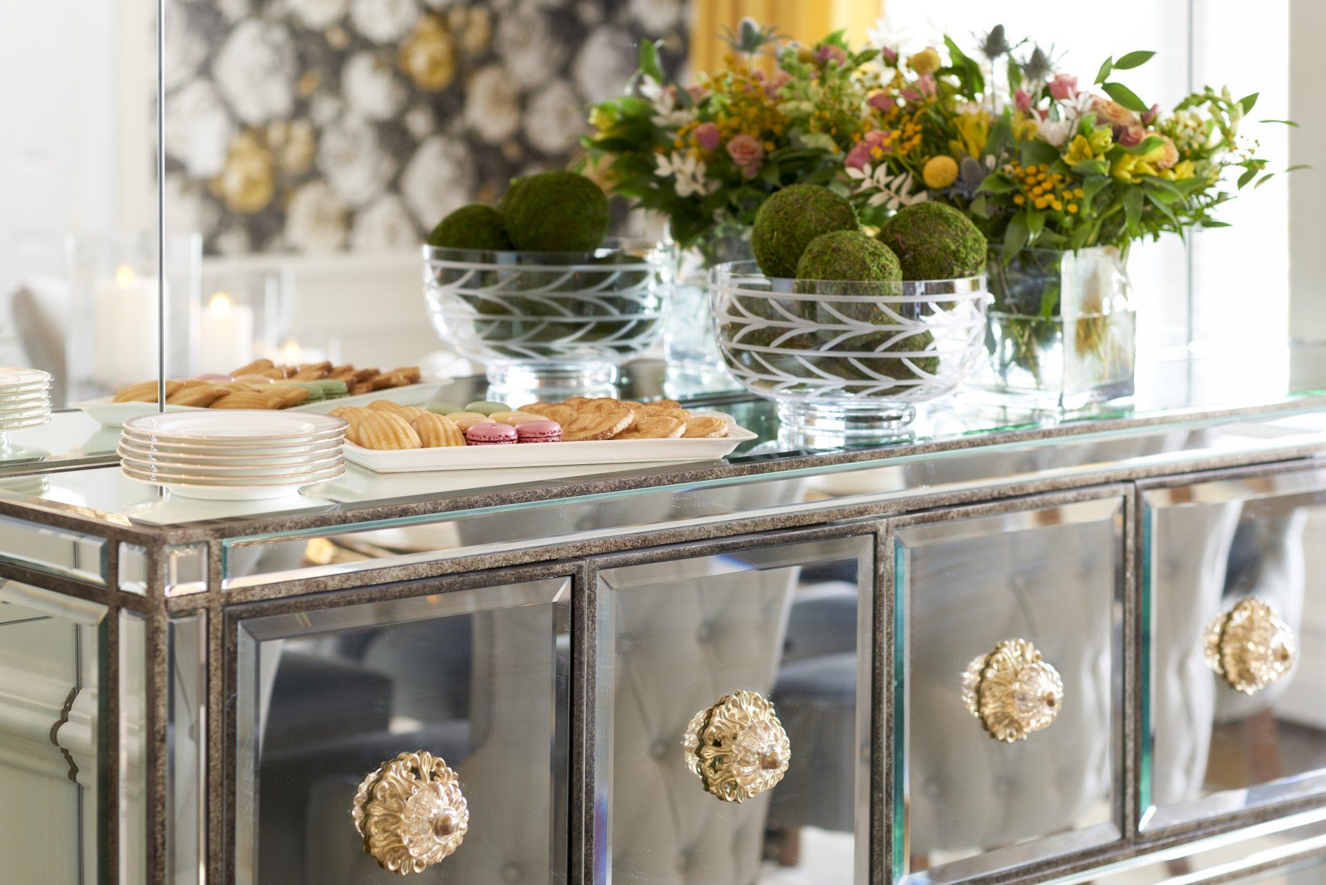 A mirrored dresser with flowers and cookies on it in a living room.