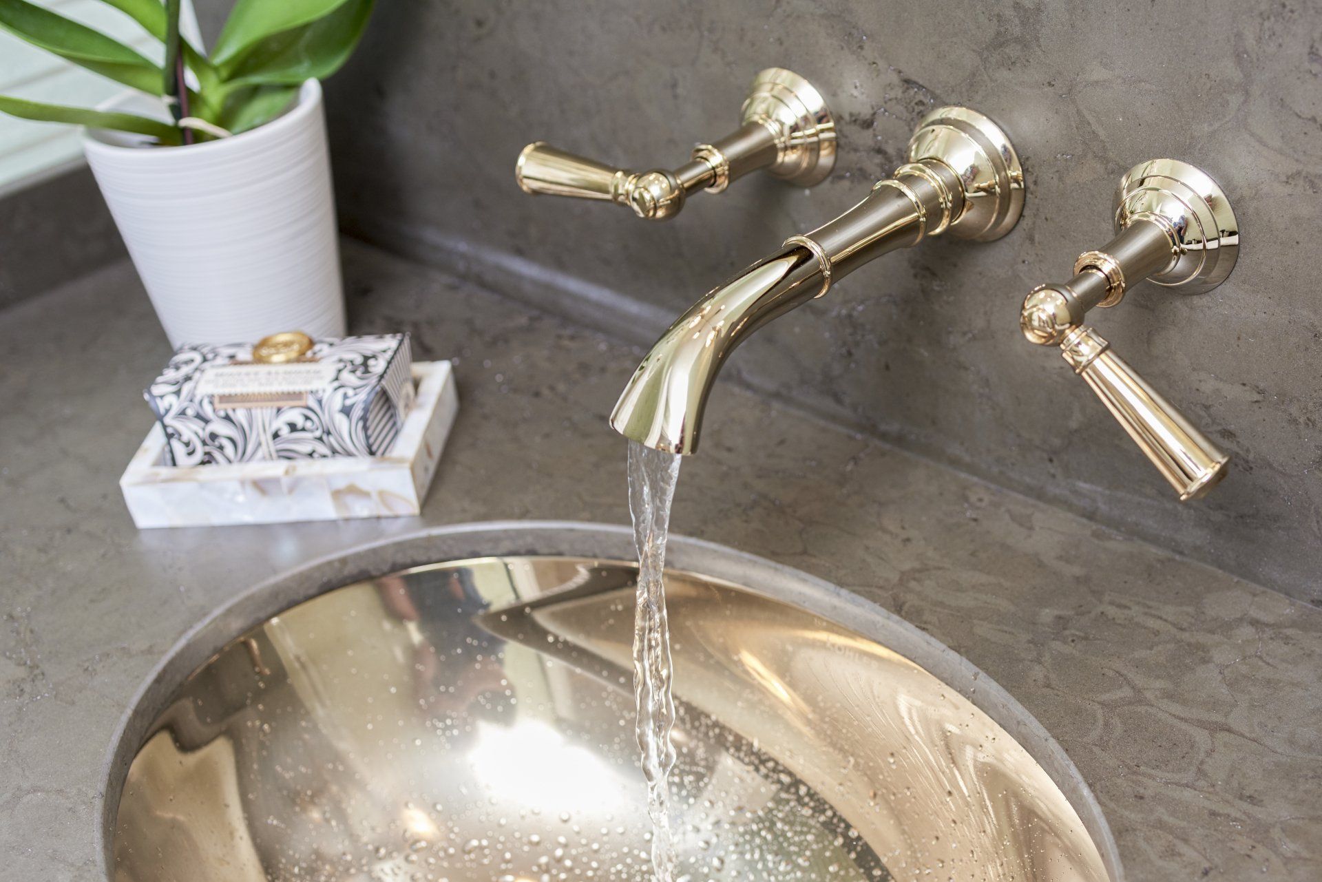 A bathroom sink with a gold faucet and a plant in the background