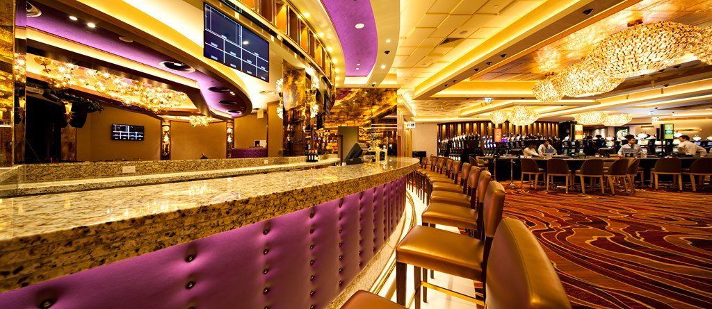 A long bar in a casino with purple chairs.