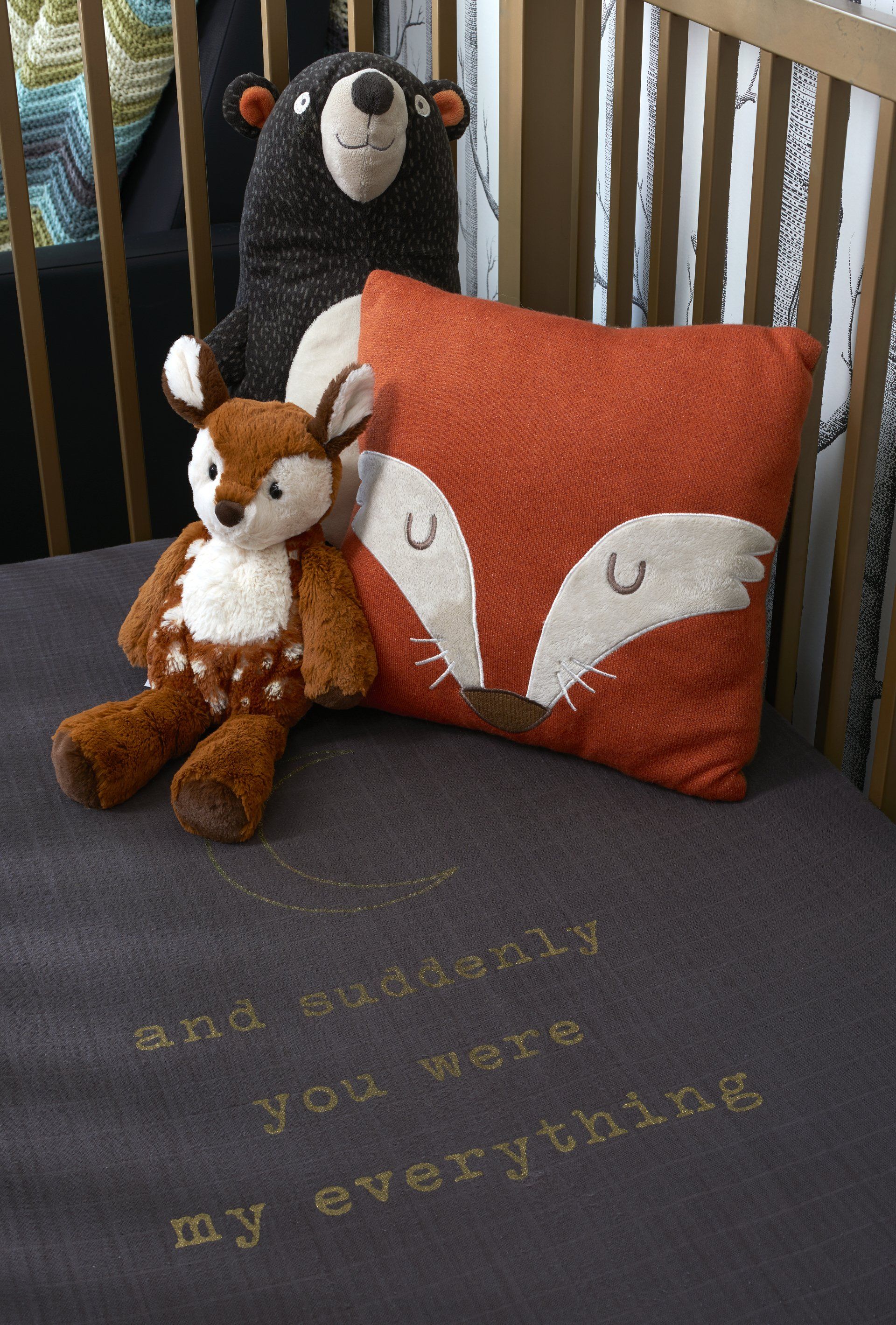 A pillow with a fox on it sits on a crib with stuffed animals