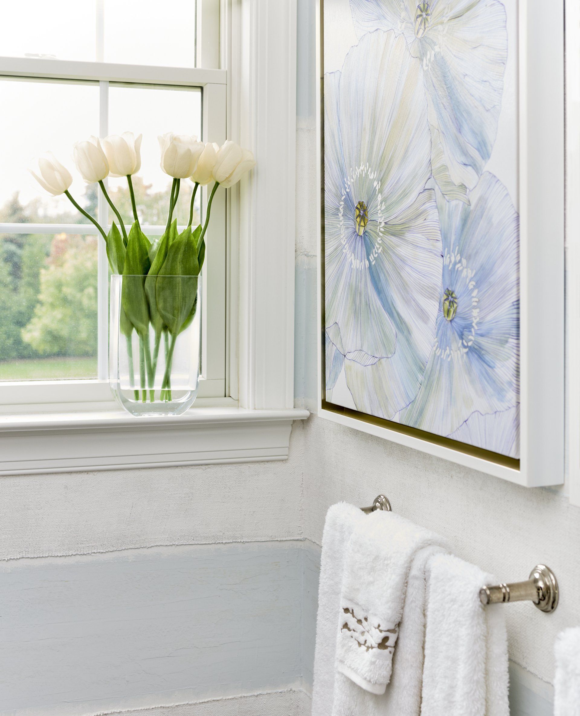 A bathroom with a vase of flowers and a painting on the wall.