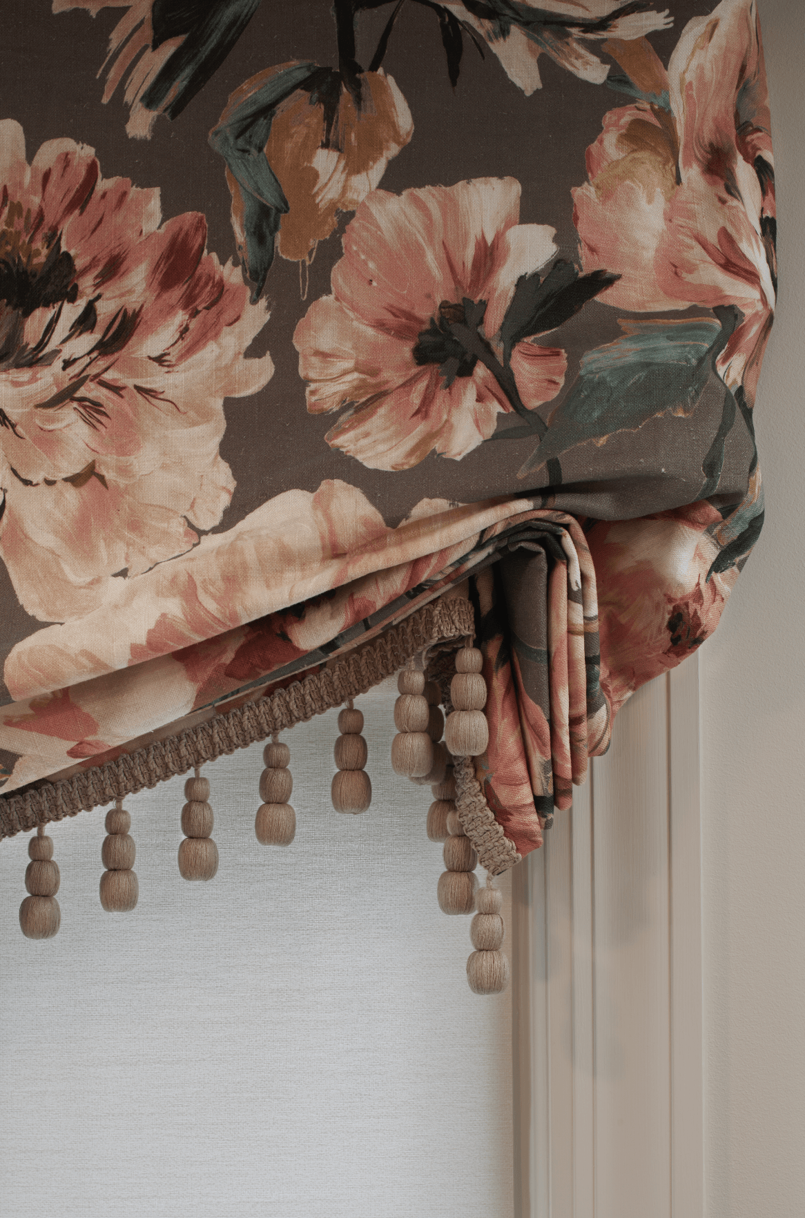 A close up of a floral roman shade with tassels on a window.