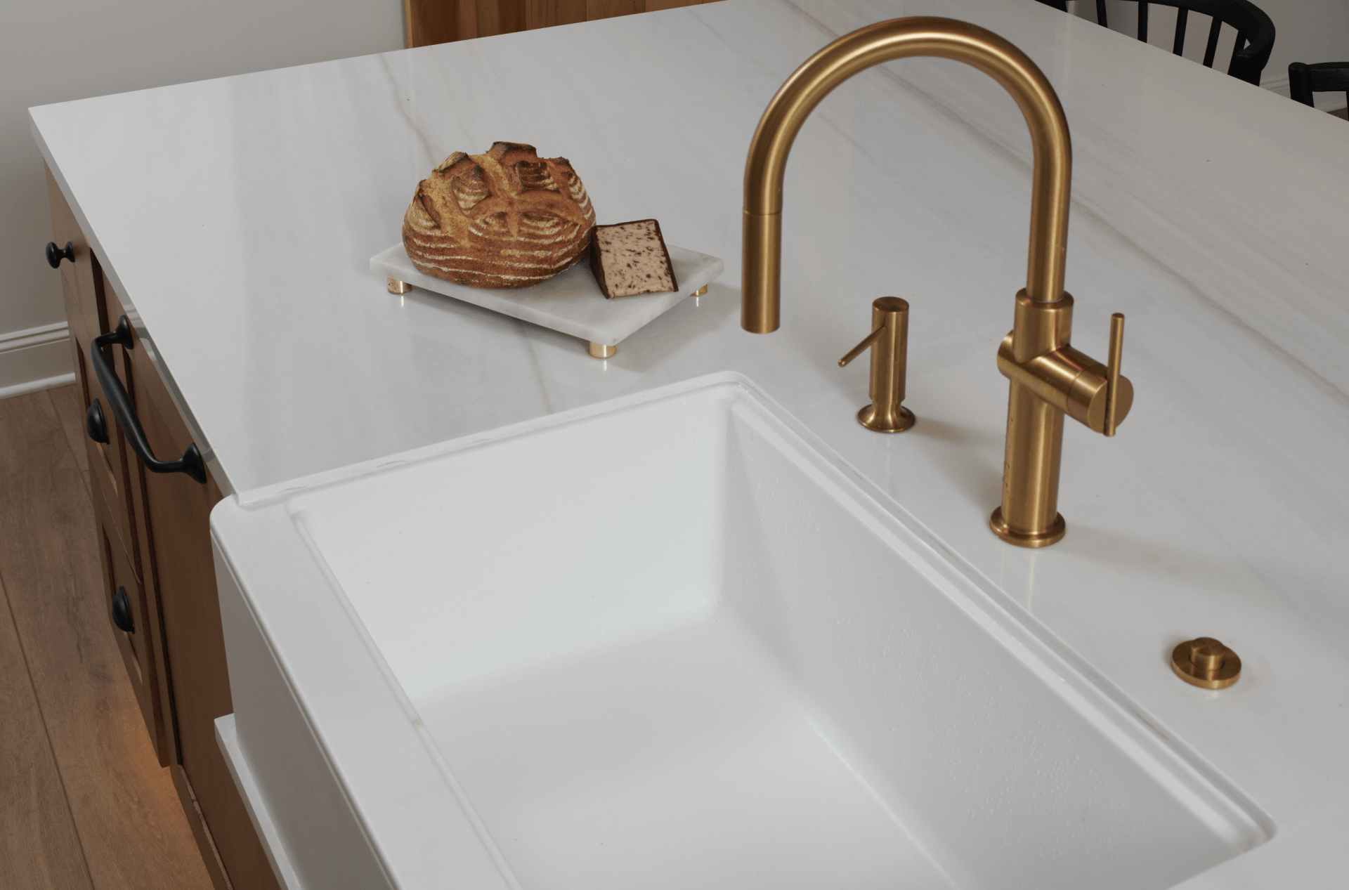 A kitchen sink with a gold faucet and a loaf of bread on the counter.