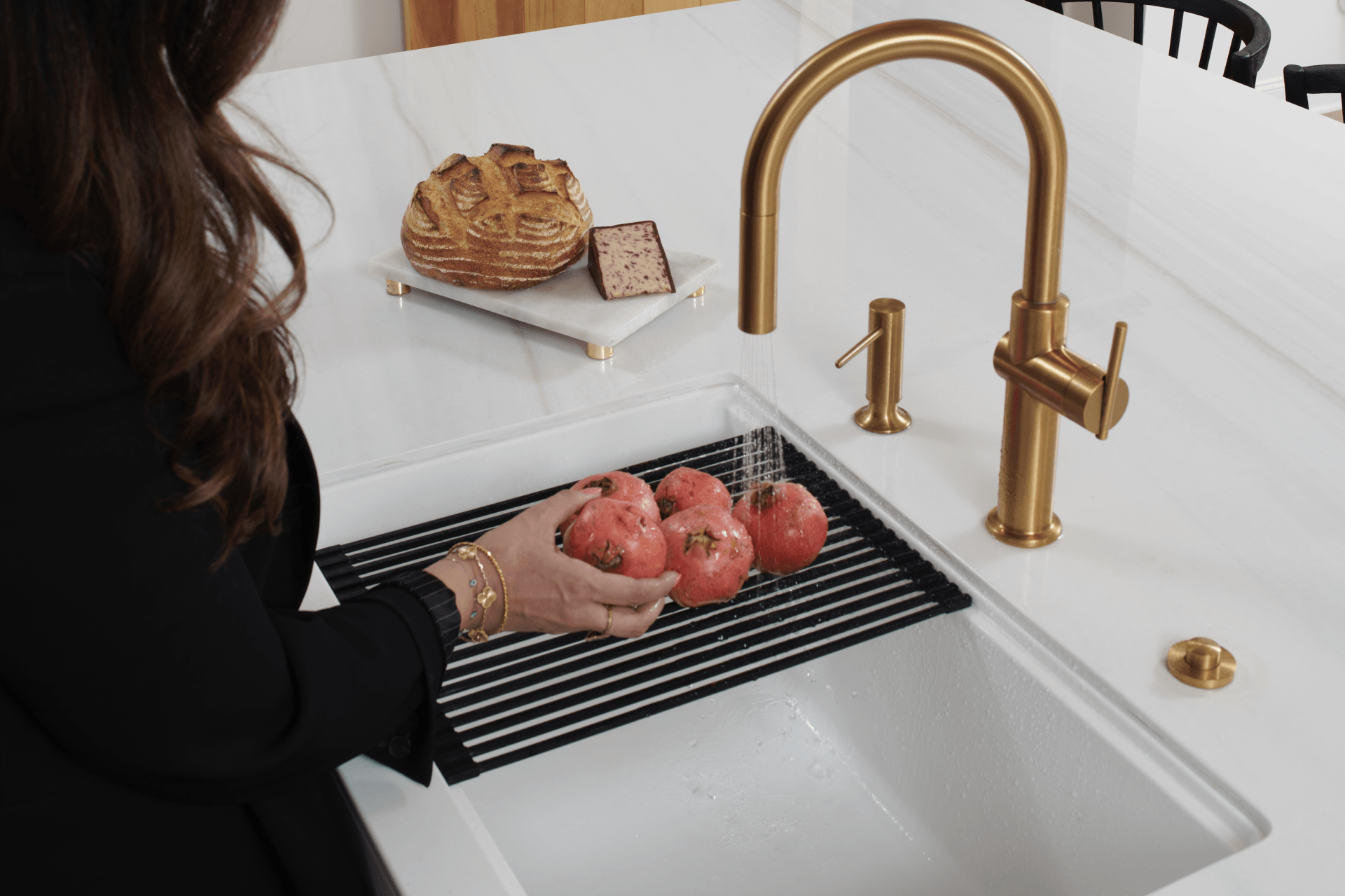 A woman is washing pomegranates in a kitchen sink.