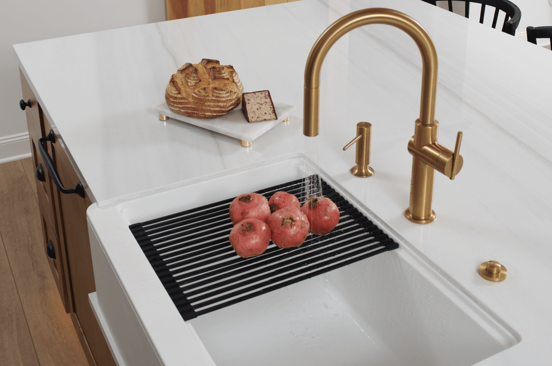 A kitchen sink with tomatoes and bread on the counter.